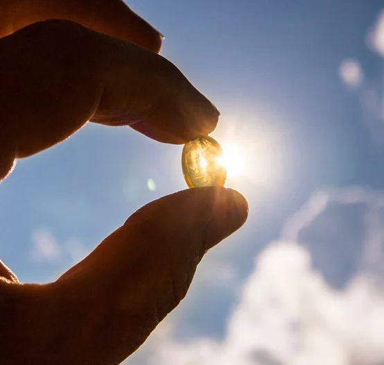Vitamin D Kapsel wird von einer Hand ins Sonnenlicht gehalten